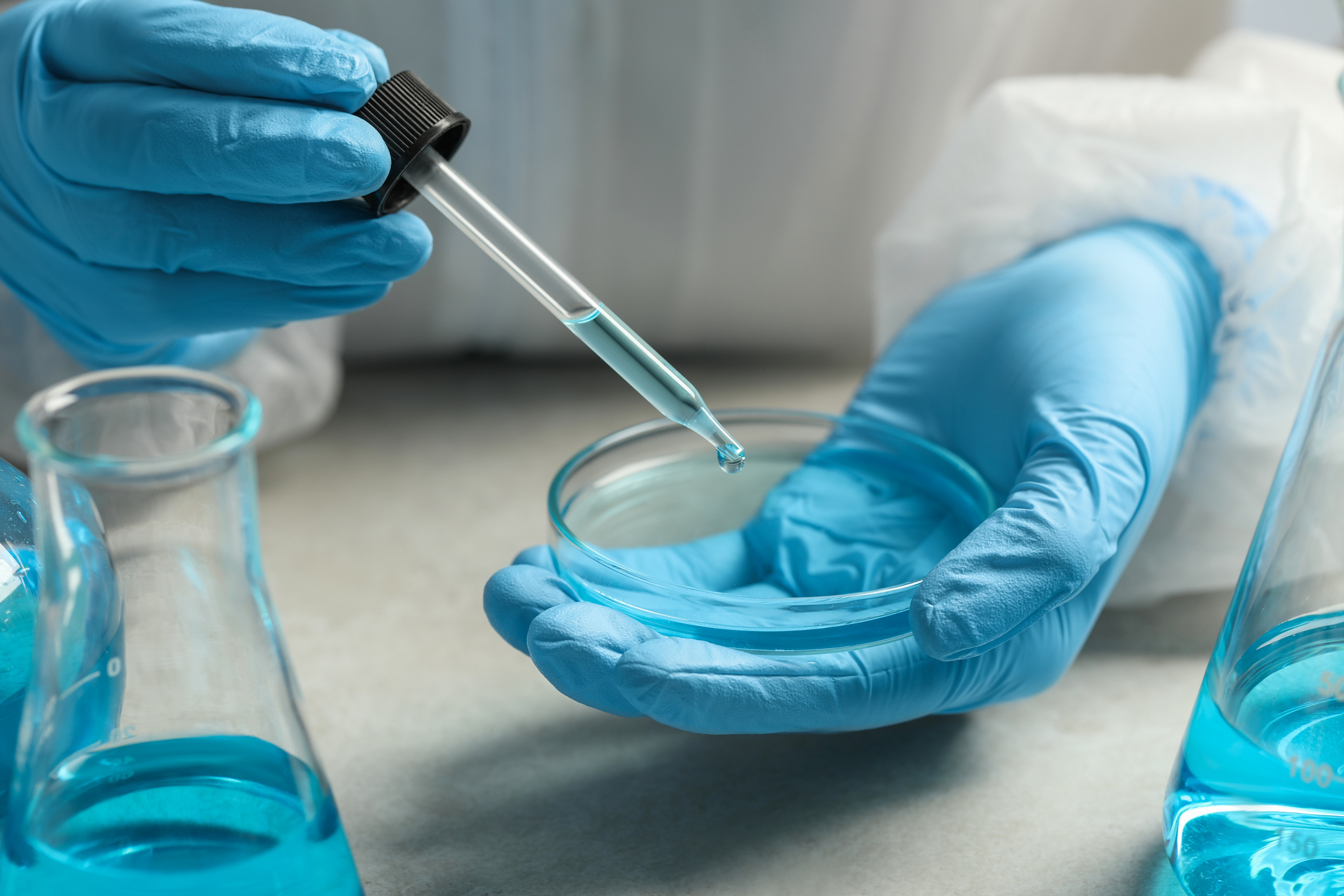 Scientist dripping liquid from pipette into petri dish at table, closeup